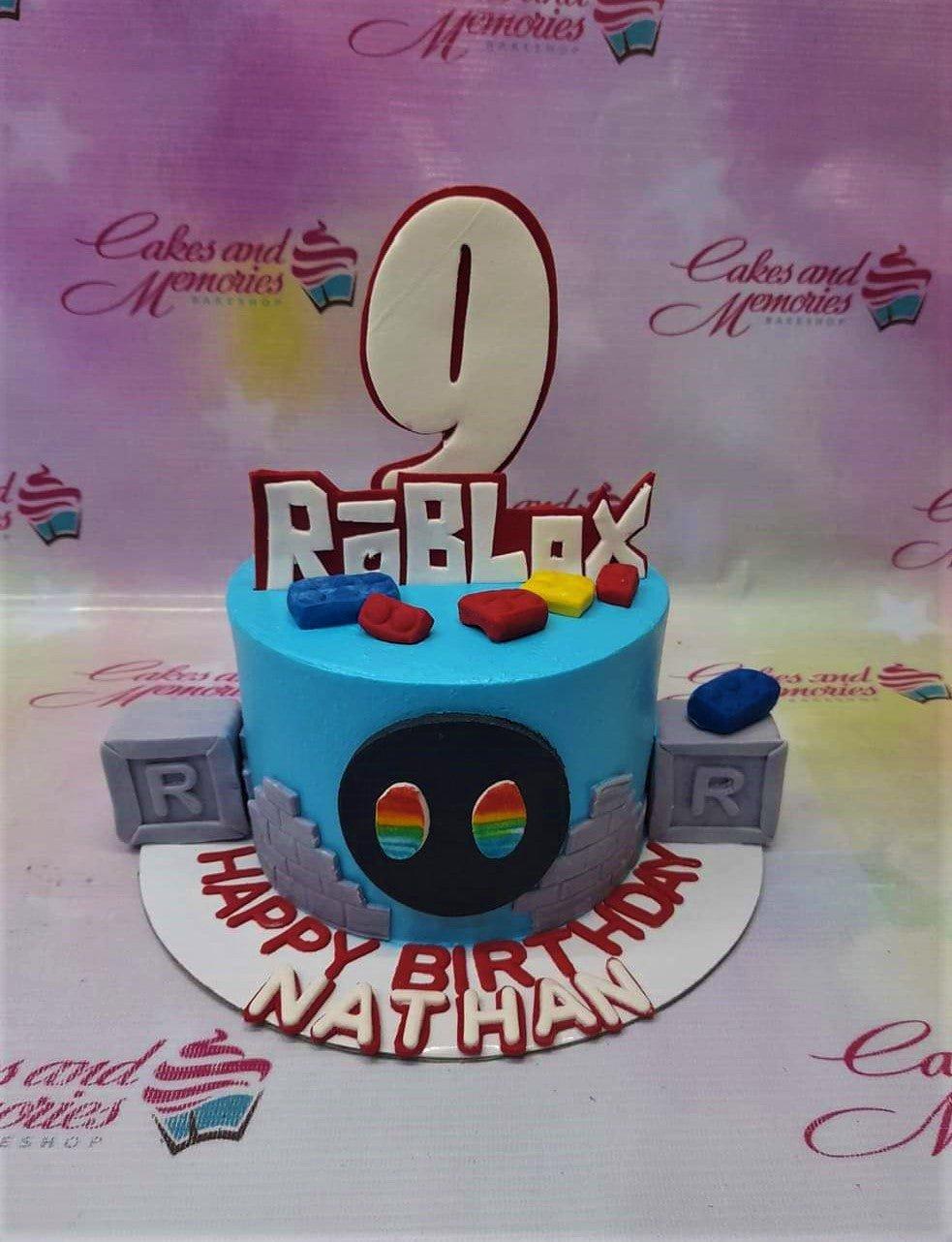 Blue Roblox themed birthday cake with a large number 9 topper, brick decorations, and a black character face on the side.