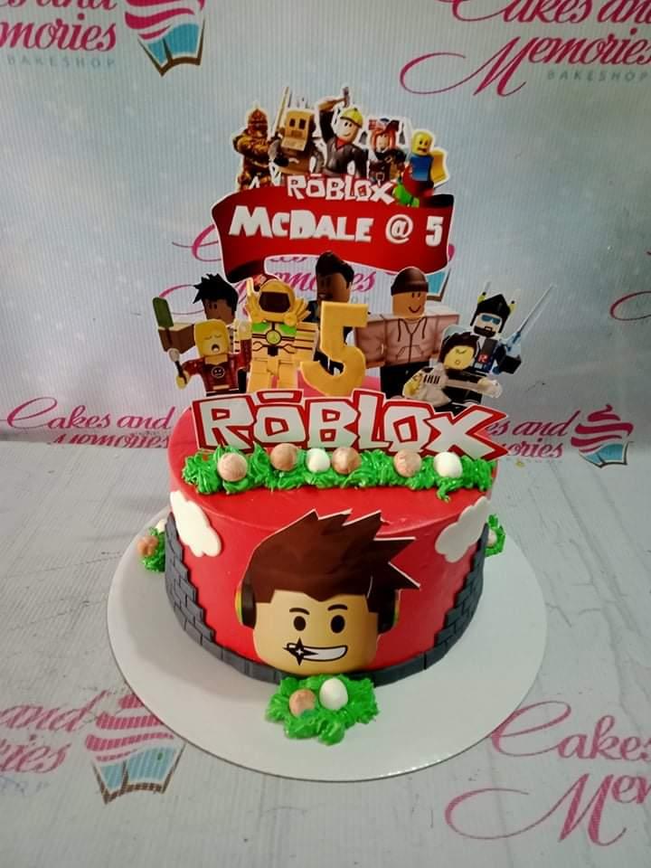 Red Roblox themed birthday cake with character printouts, green icing grass, and a custom name banner for McDale's 5th birthday.
