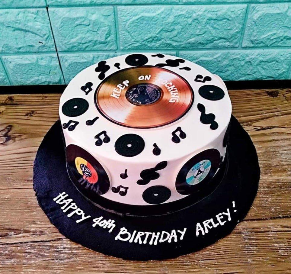 White round music themed cake with vinyl record printouts and black icing musical notes on a black base board.