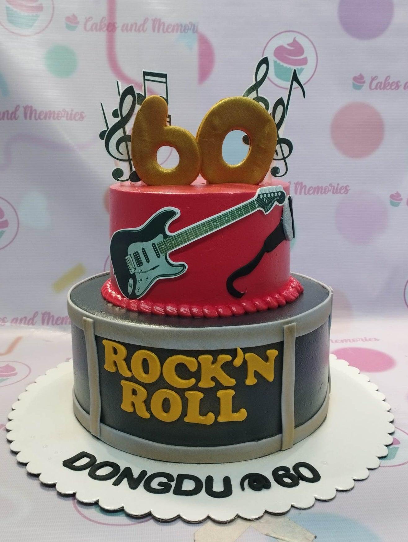 Two-tier rock and roll themed cake with a red top tier featuring a guitar and a black bottom tier designed like a drum with 'ROCK'N ROLL' text.