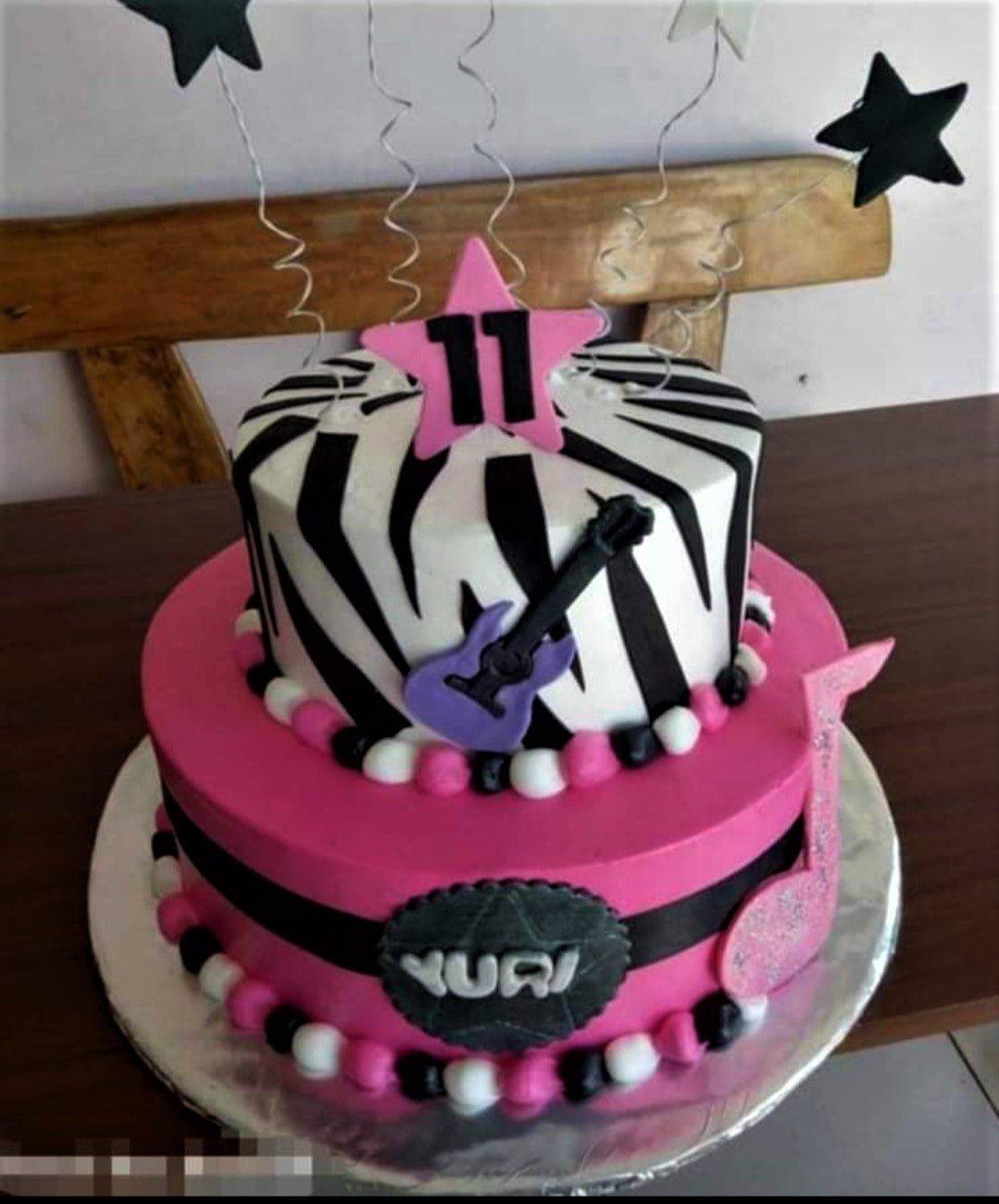 Two-tier pink and zebra print rockstar birthday cake with a purple guitar, music notes, and star toppers for an 11th birthday.