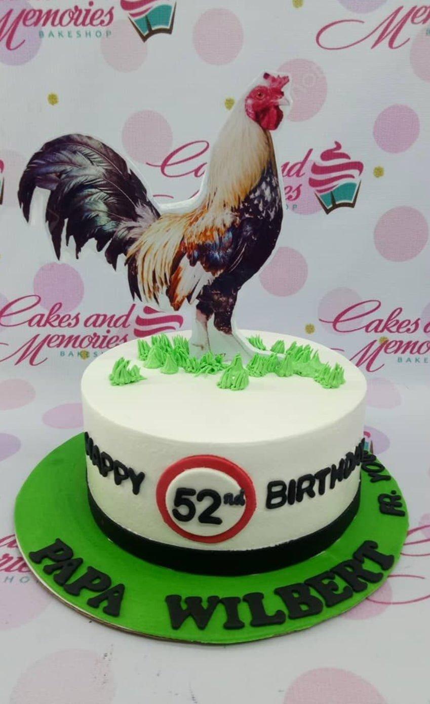 White round birthday cake for Papa Wilbert featuring a large rooster printout topper and green icing grass accents on a green base board.