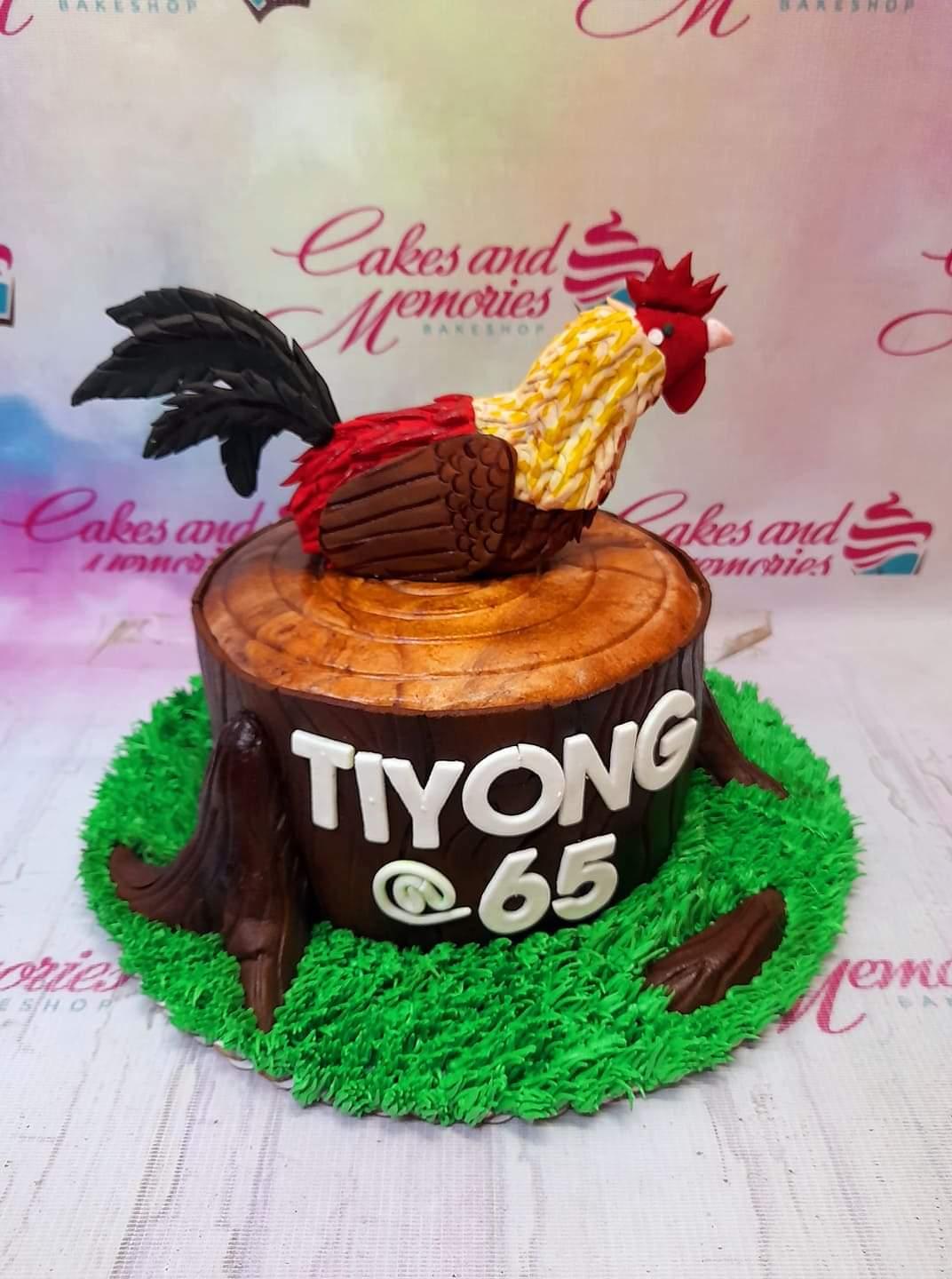 A brown tree stump cake with a detailed fondant rooster topper and green icing grass base.