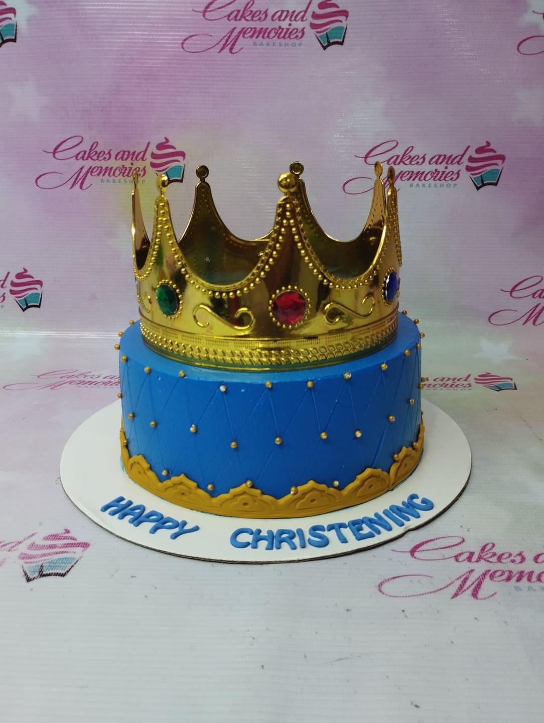 Blue 1-tier christening cake with a large gold crown topper and quilted icing pattern with gold beads.