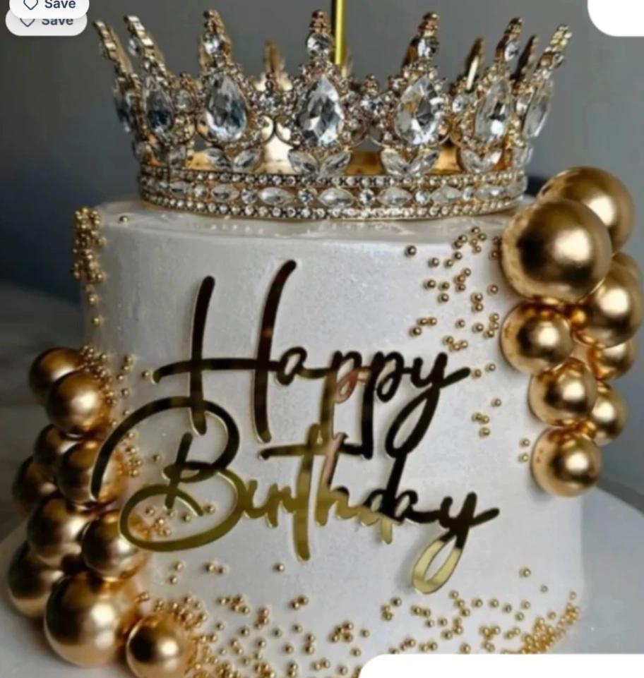 White textured cake with a large gold rhinestone crown on top, gold spheres on the sides, and a gold Happy Birthday topper.