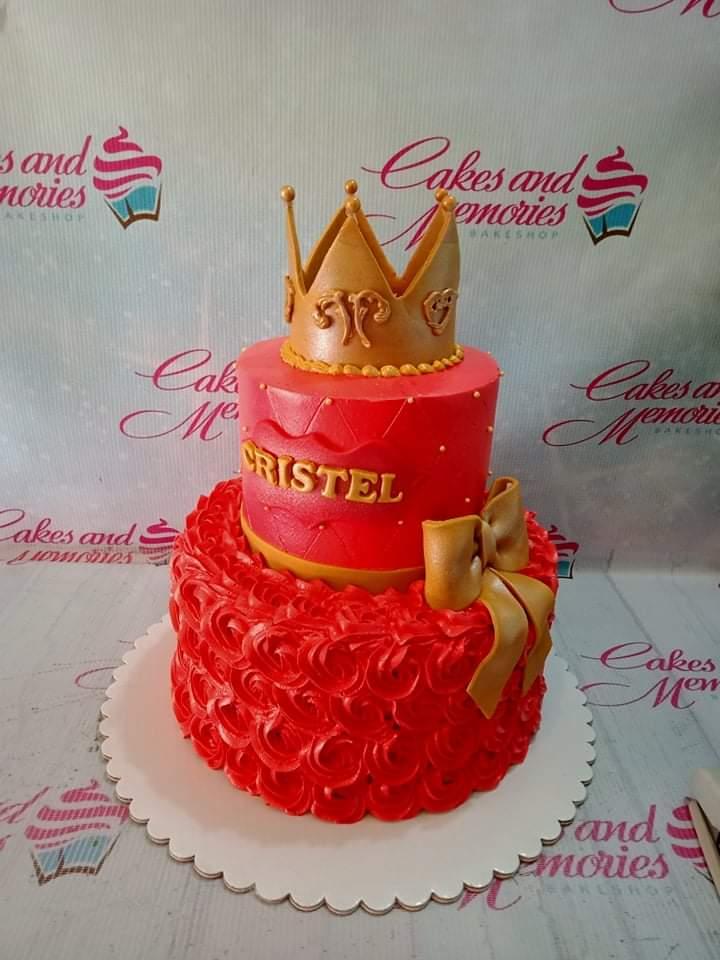 Red two-tier royal crown cake with gold bow and icing rosettes