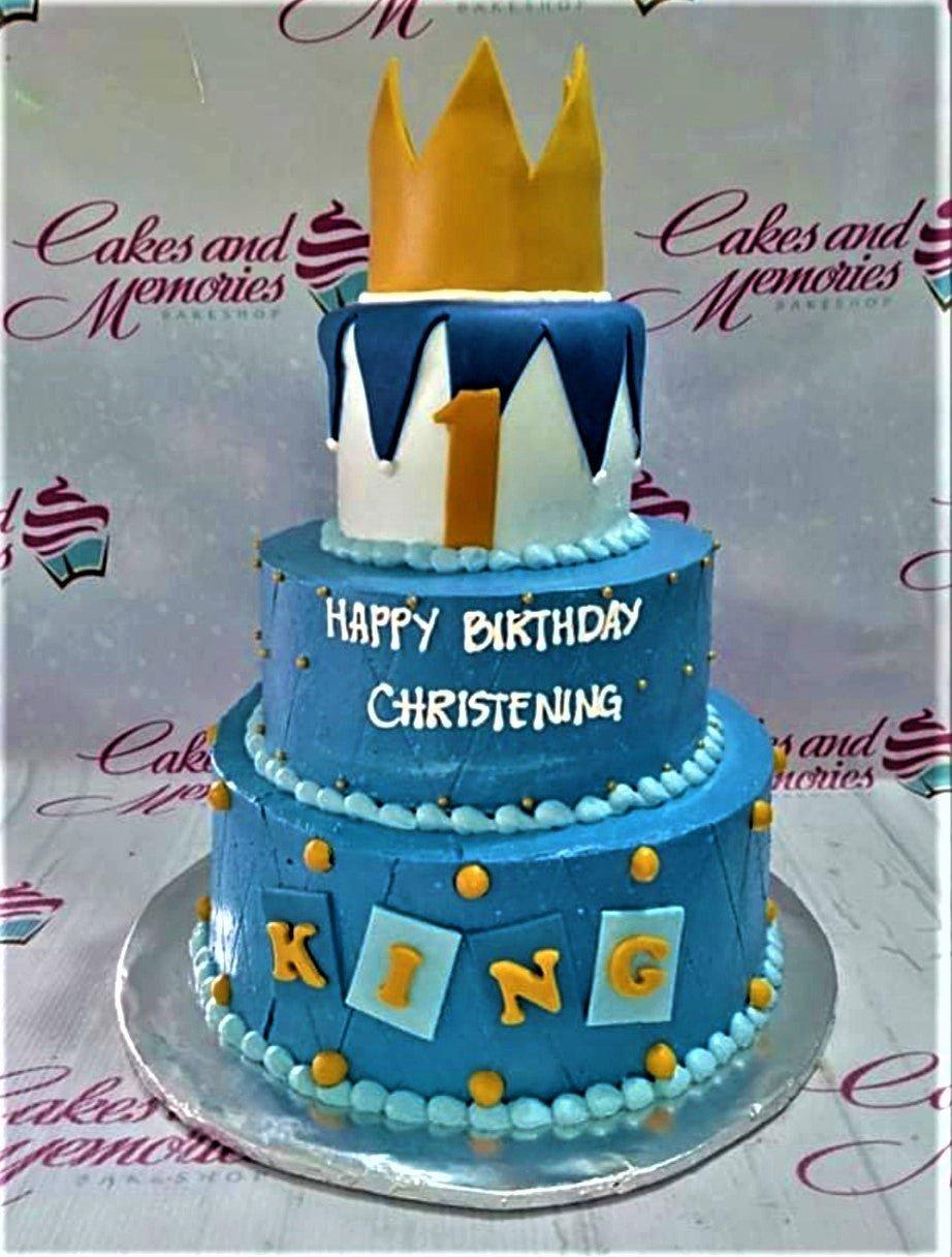 Three-tier blue and white royal crown cake with gold accents and personalized name blocks for a christening and birthday celebration.