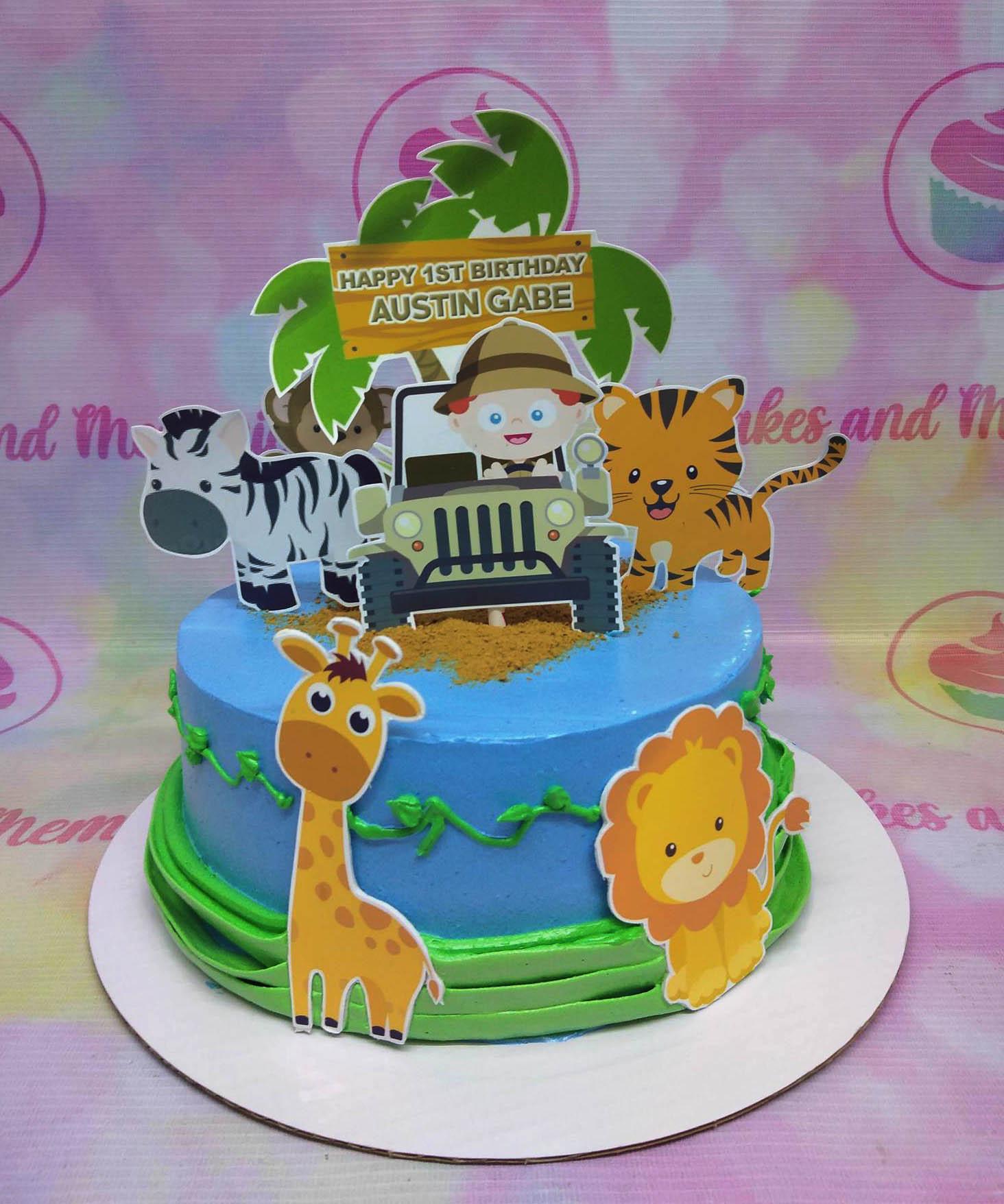 Blue safari themed birthday cake with printed animal toppers including a giraffe, lion, zebra, and tiger with a jeep and palm tree.