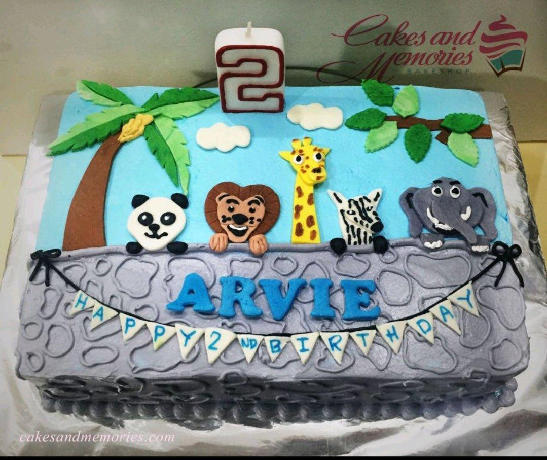 Rectangle blue safari birthday cake with fondant animals including a panda, lion, giraffe, zebra, and elephant with a number 2 candle.
