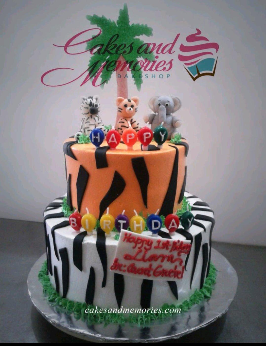 Two-tier safari themed cake with orange tiger stripes and white zebra stripes, featuring fondant elephant, tiger, and zebra figures.