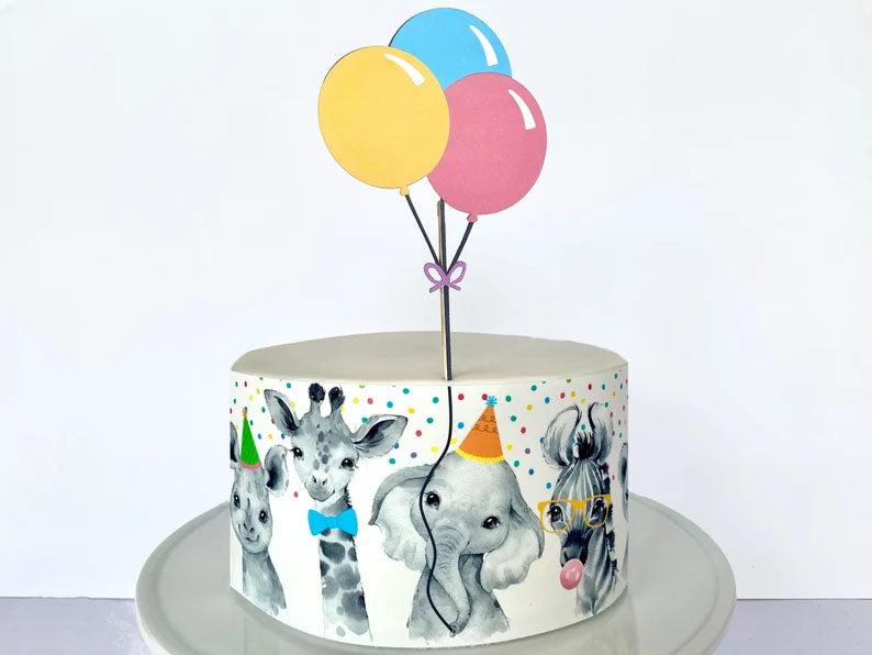 White single tier birthday cake featuring a wrap-around animal printout with a giraffe, elephant, and zebra wearing party hats and glasses.