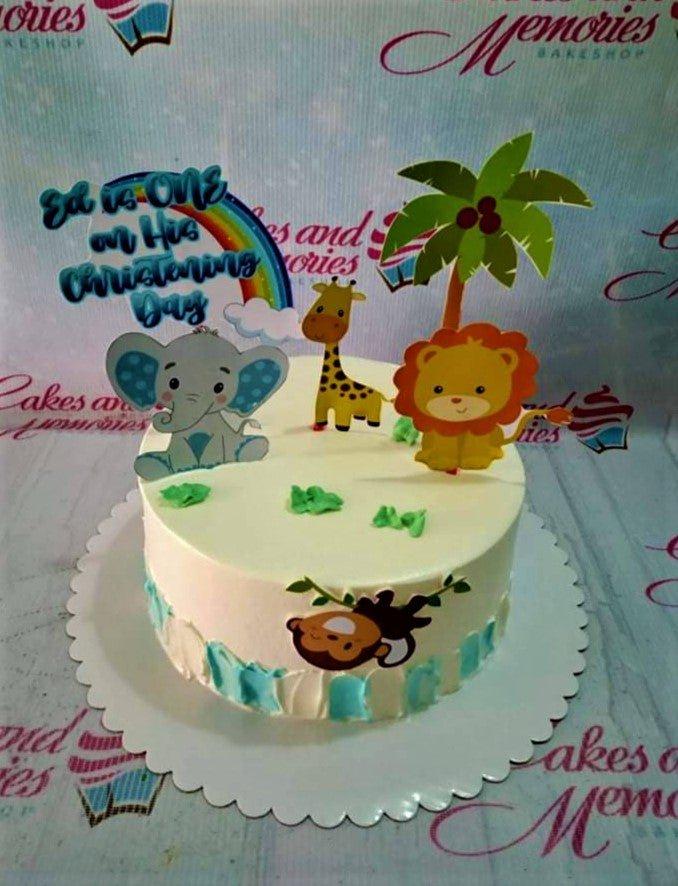 White 1-tier safari themed christening cake with printout toppers of an elephant, giraffe, lion, and palm tree with blue icing accents.