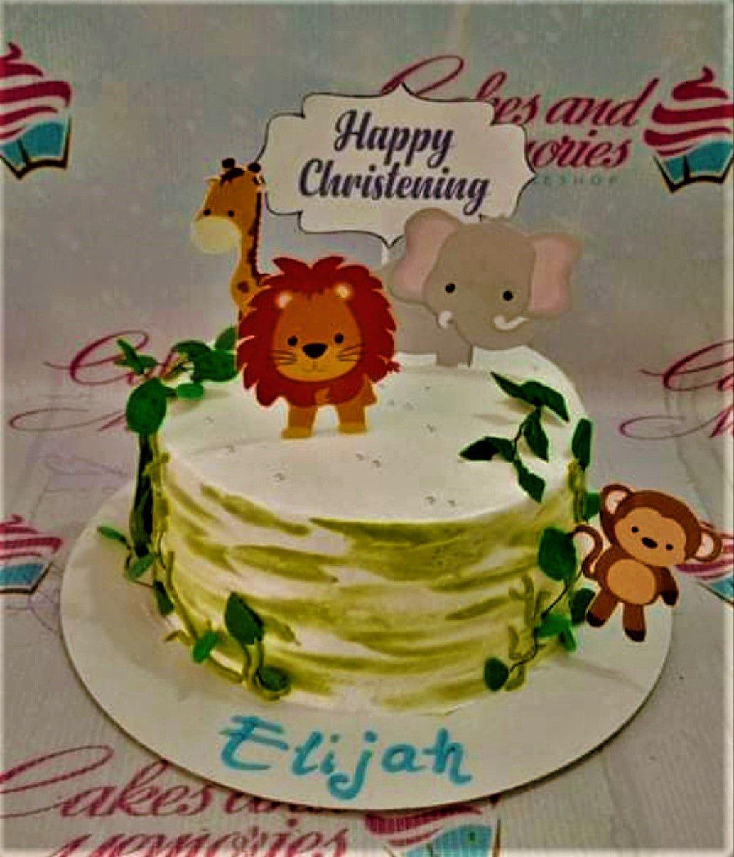 White 1-tier christening cake with green leaf icing details and safari animal printout toppers including a lion, giraffe, and elephant.