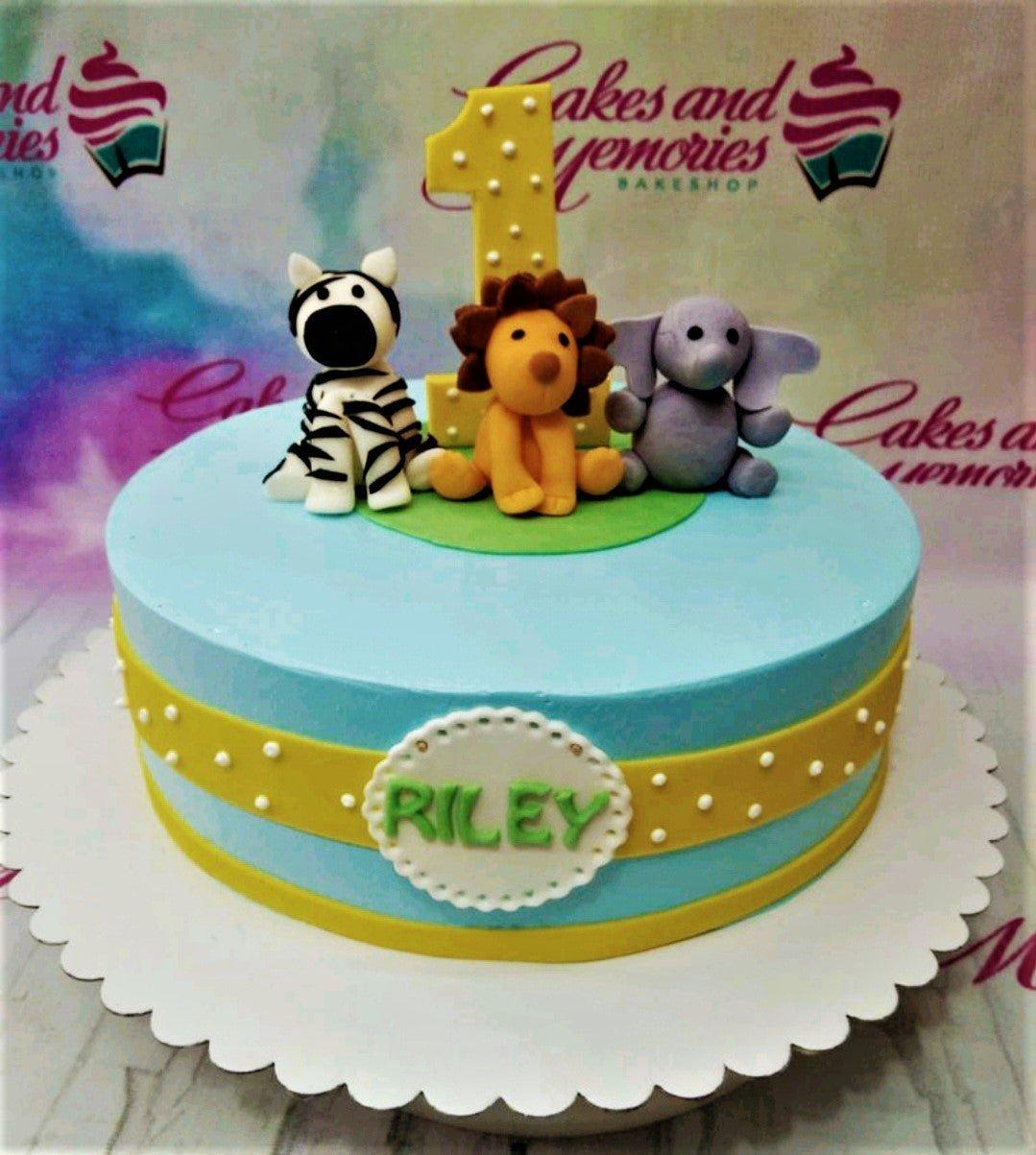 Light blue 1-tier safari birthday cake with fondant lion, zebra, and elephant figures and a yellow number one topper.