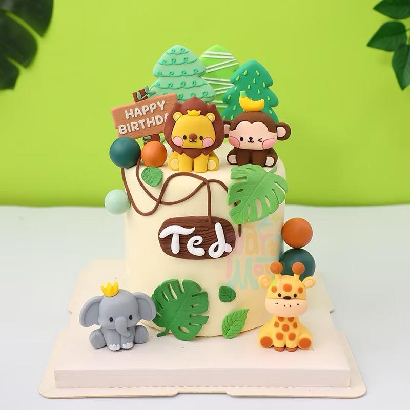 A pale yellow 6-inch cake featuring a fondant lion, monkey, elephant, giraffe, jungle trees, a 'Happy Birthday' sign, and a name plaque.