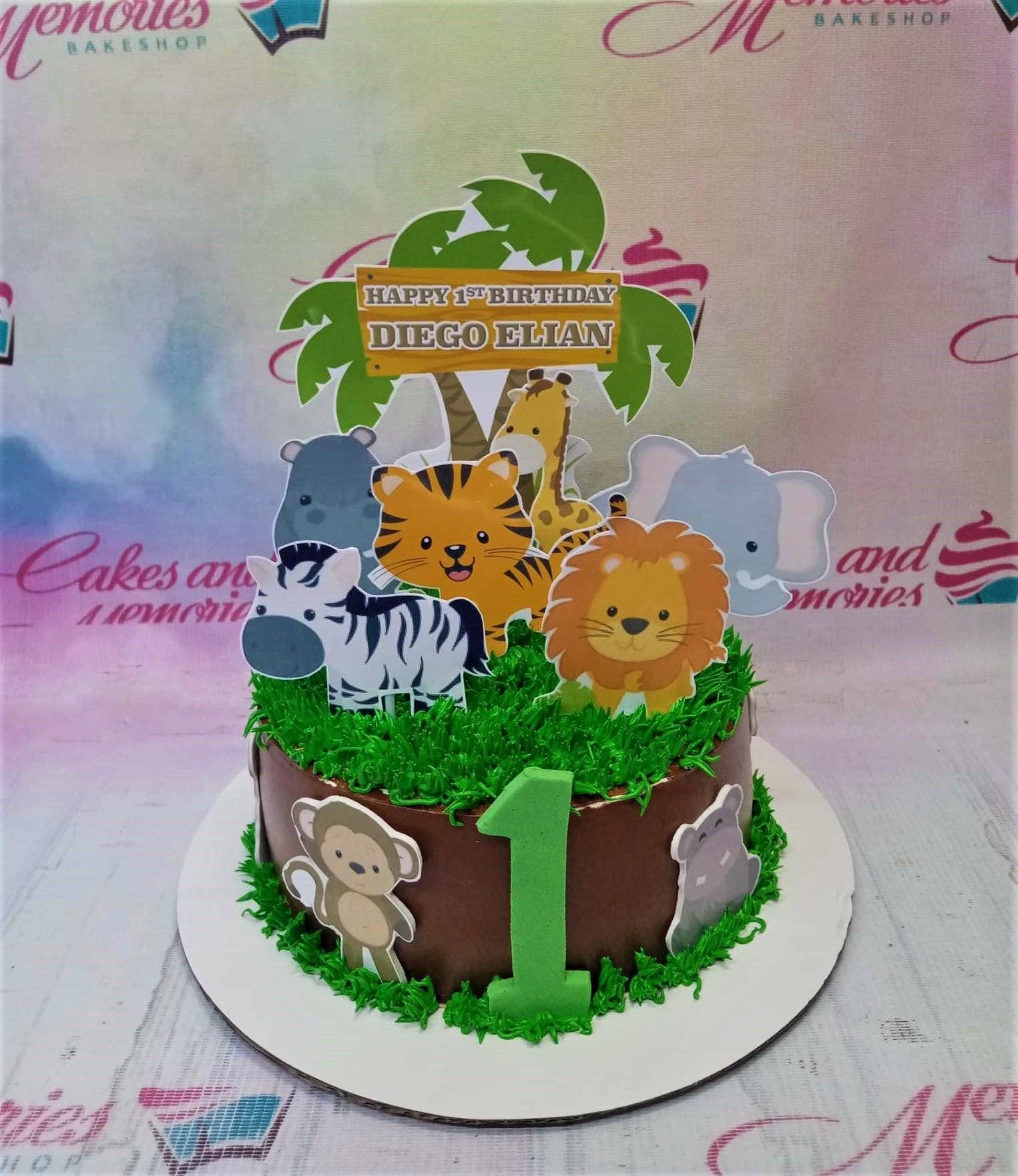 Chocolate brown safari birthday cake with green grass icing, a large green number one, and various jungle animal printouts.