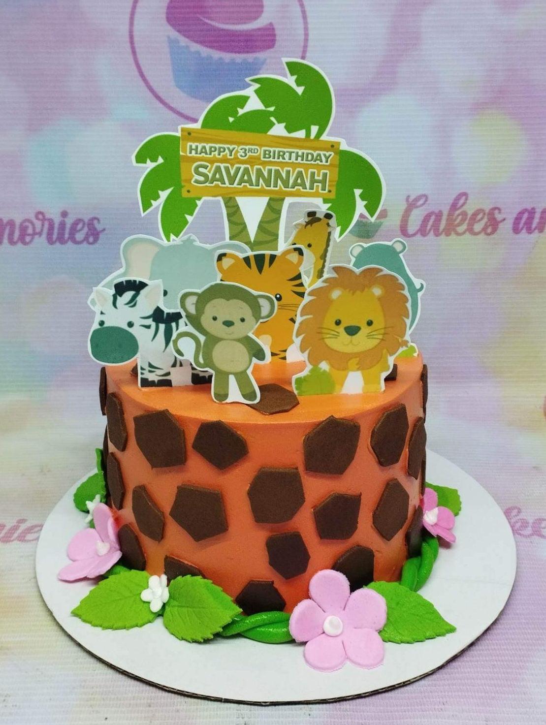 Orange safari themed birthday cake with giraffe print patterns, jungle animal printouts, and pink fondant flowers.