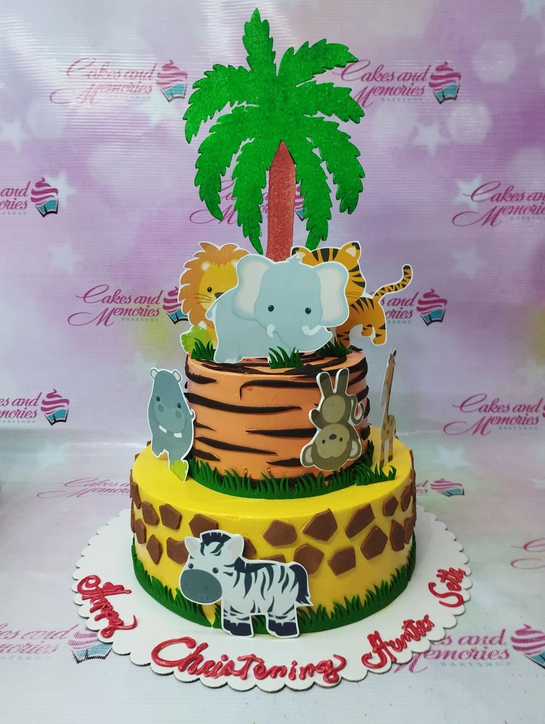 Two-tier safari animal themed cake with orange tiger stripes and yellow giraffe patterns, topped with a large palm tree and jungle animal cutouts.