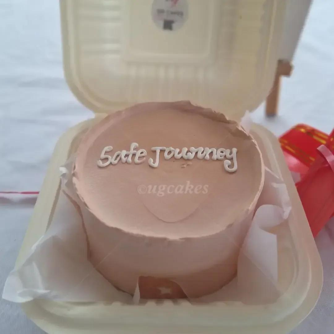 Minimalist peach bento cake with white piped icing message 'Safe Journey' in a white takeout container.