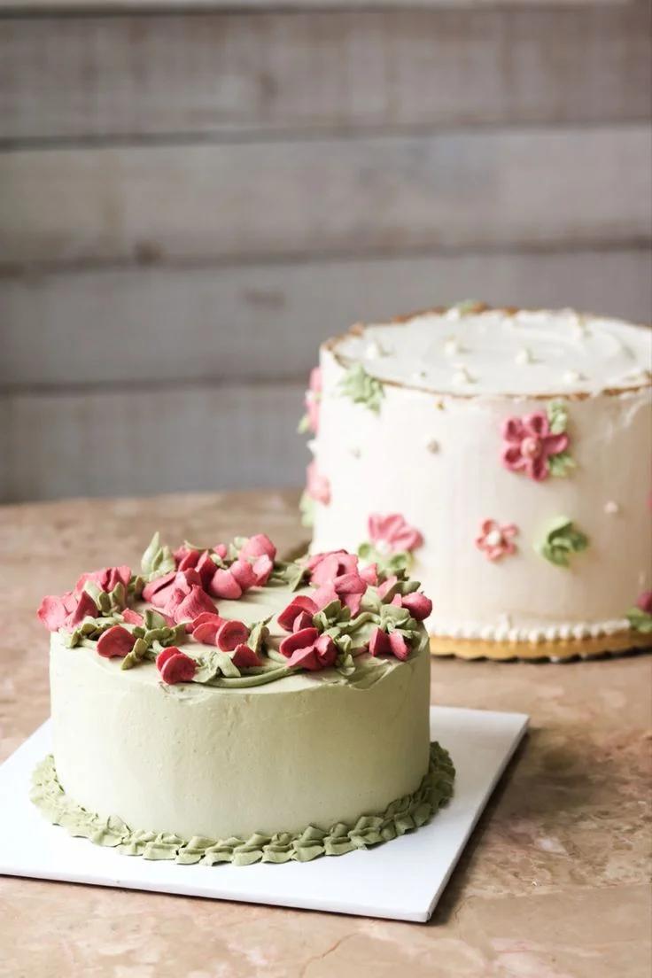 A minimalist sage green cake with pink and green piped icing flowers on top and a ruffled border at the base.