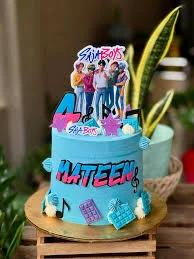 Blue K-pop themed cake with Saja Boys character printouts, musical notes, and blue icing rosettes on a gold base.