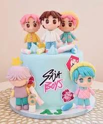 Light blue fondant cake featuring five 3D boy figurines with colorful hair, marshmallows, and a 'Saja Boys' logo.