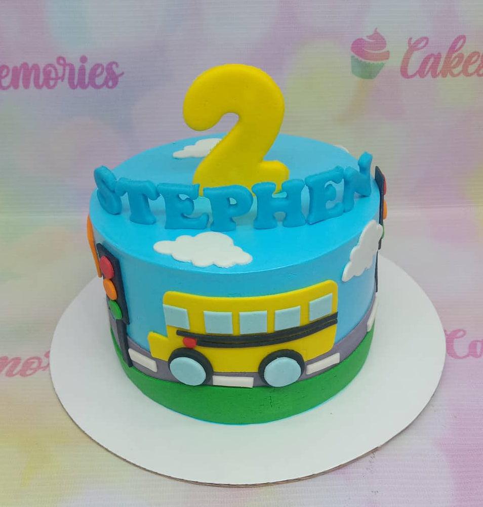 Blue school bus themed birthday cake with a yellow bus, traffic lights, and a large yellow number 2 topper for Stephen.