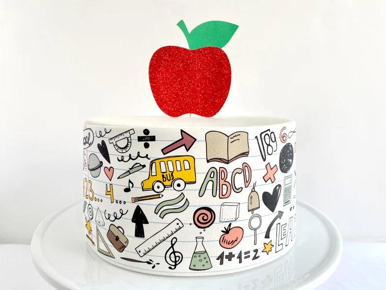 White fondant cake with school-themed doodles and a large red glitter apple topper.