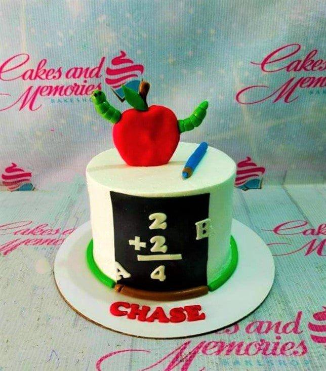White school themed birthday cake with a large red fondant apple, a green worm, a blue pencil, and a chalkboard design.