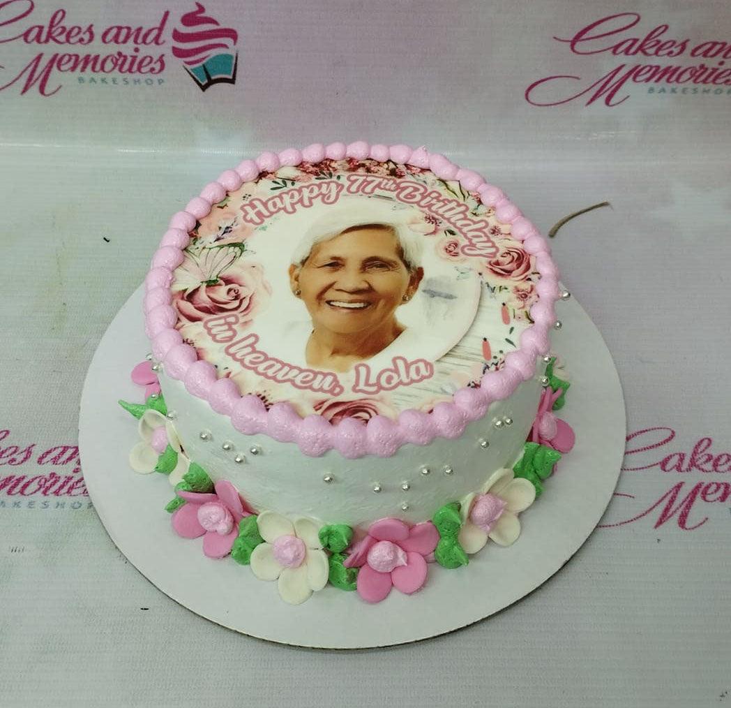 White 1-tier memorial cake with a large edible photo print of a woman, pink icing rosettes, and pink and white fondant flowers.