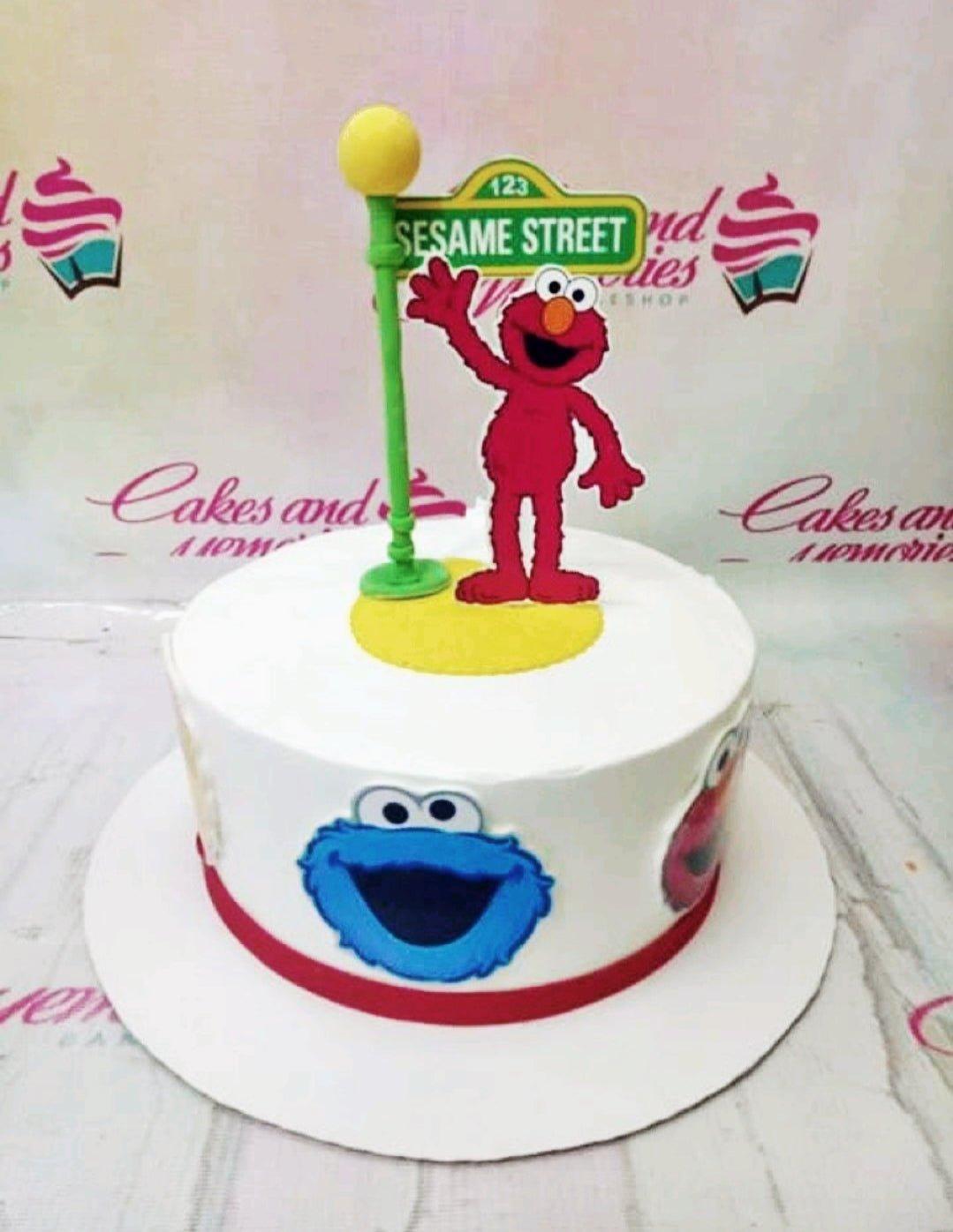 White 1-tier Sesame Street birthday cake featuring Elmo and Cookie Monster printouts with a street lamp topper.