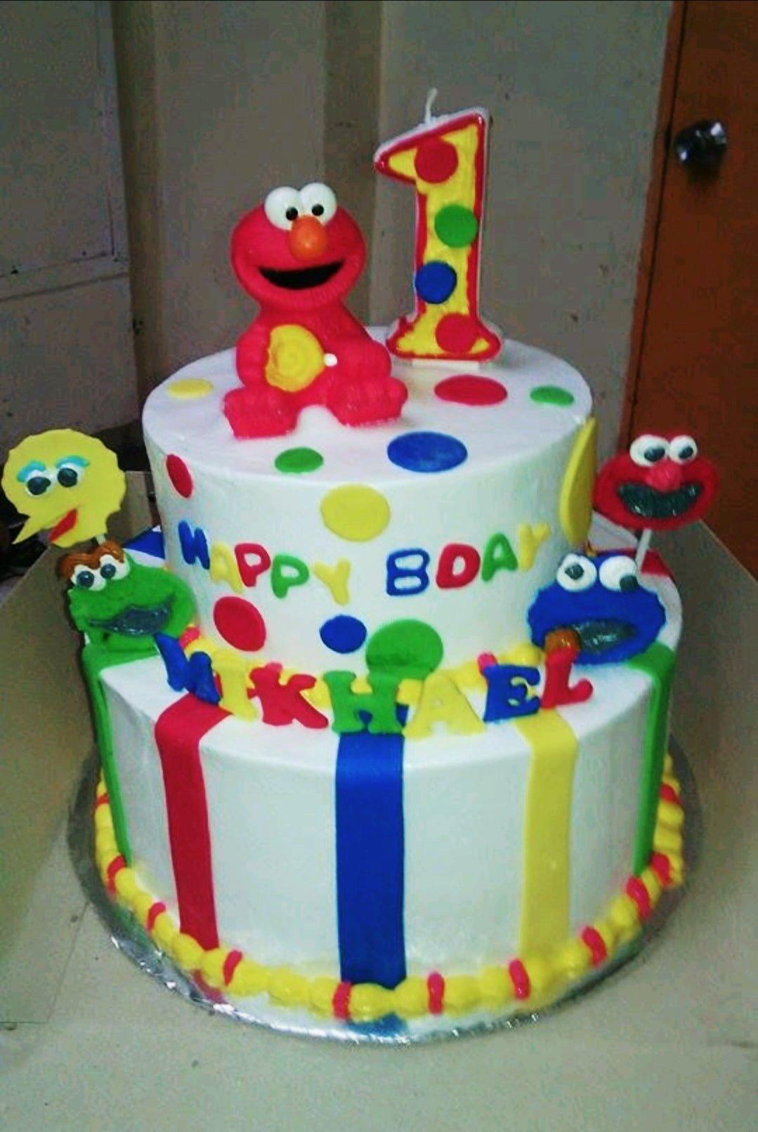 Two-tier Sesame Street themed birthday cake with Elmo, Cookie Monster, and Big Bird fondant figures and colorful stripes.