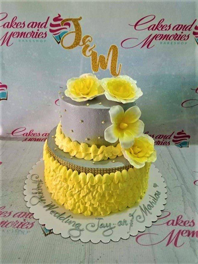 Two-tier silver and yellow wedding cake with large yellow gumpaste roses and a gold glitter J&M topper.