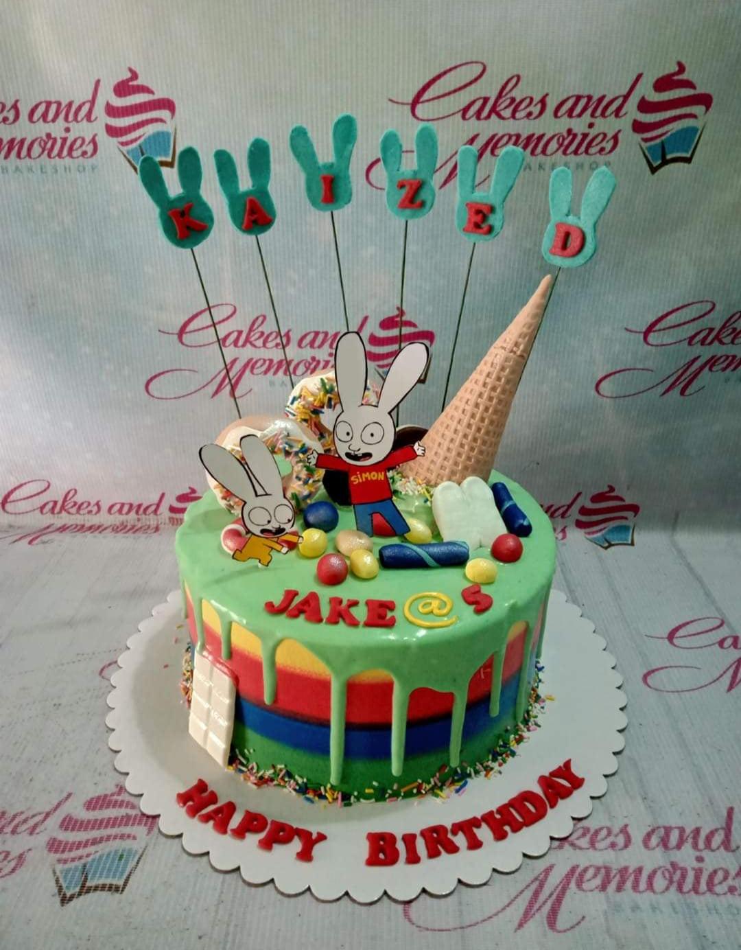 Colorful Simon the Rabbit themed birthday cake with rainbow stripes, green drip icing, and various candy toppers.
