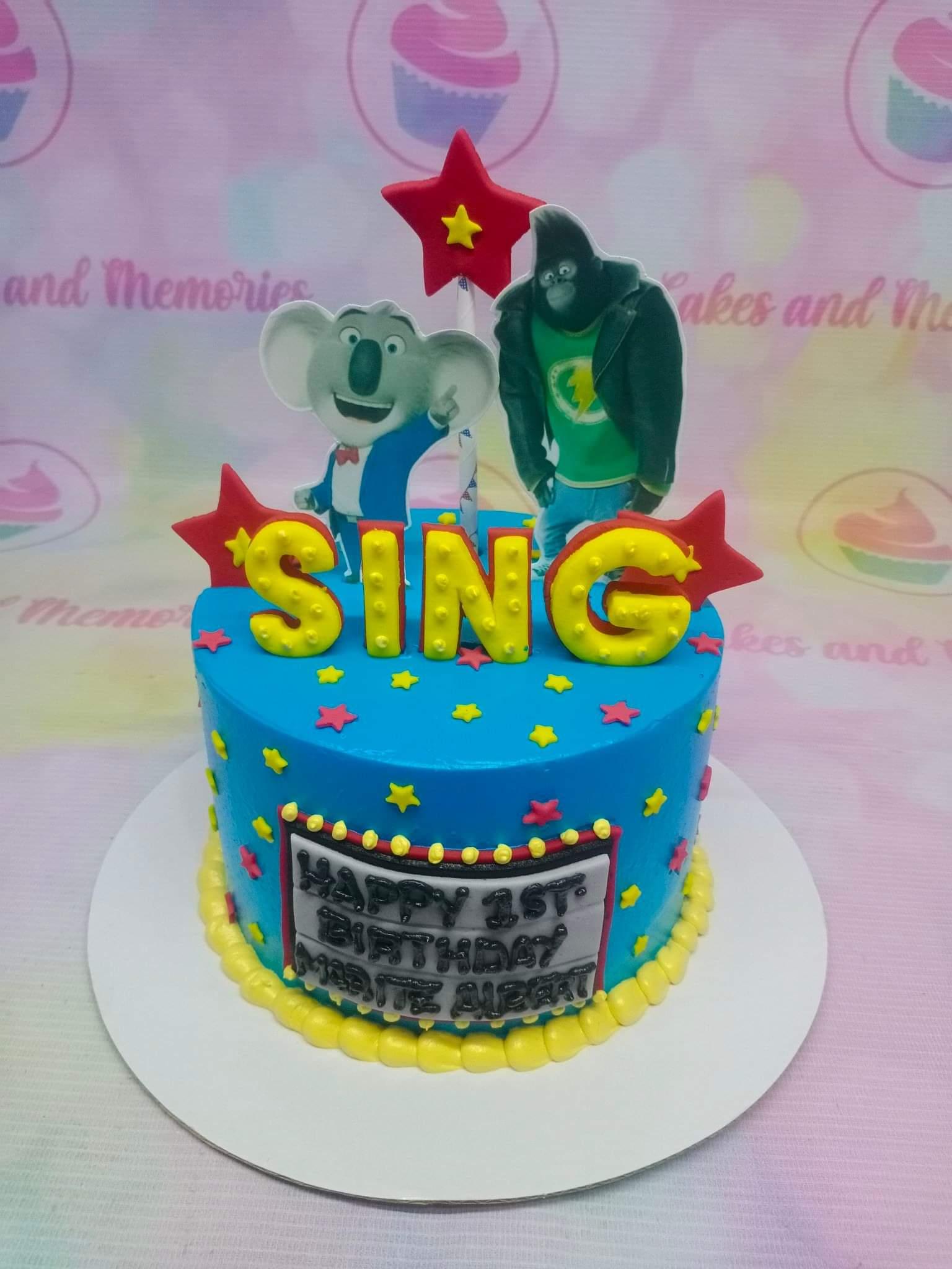 Blue Sing movie themed birthday cake with Buster Moon and Johnny printouts, yellow marquee letters, and red stars.