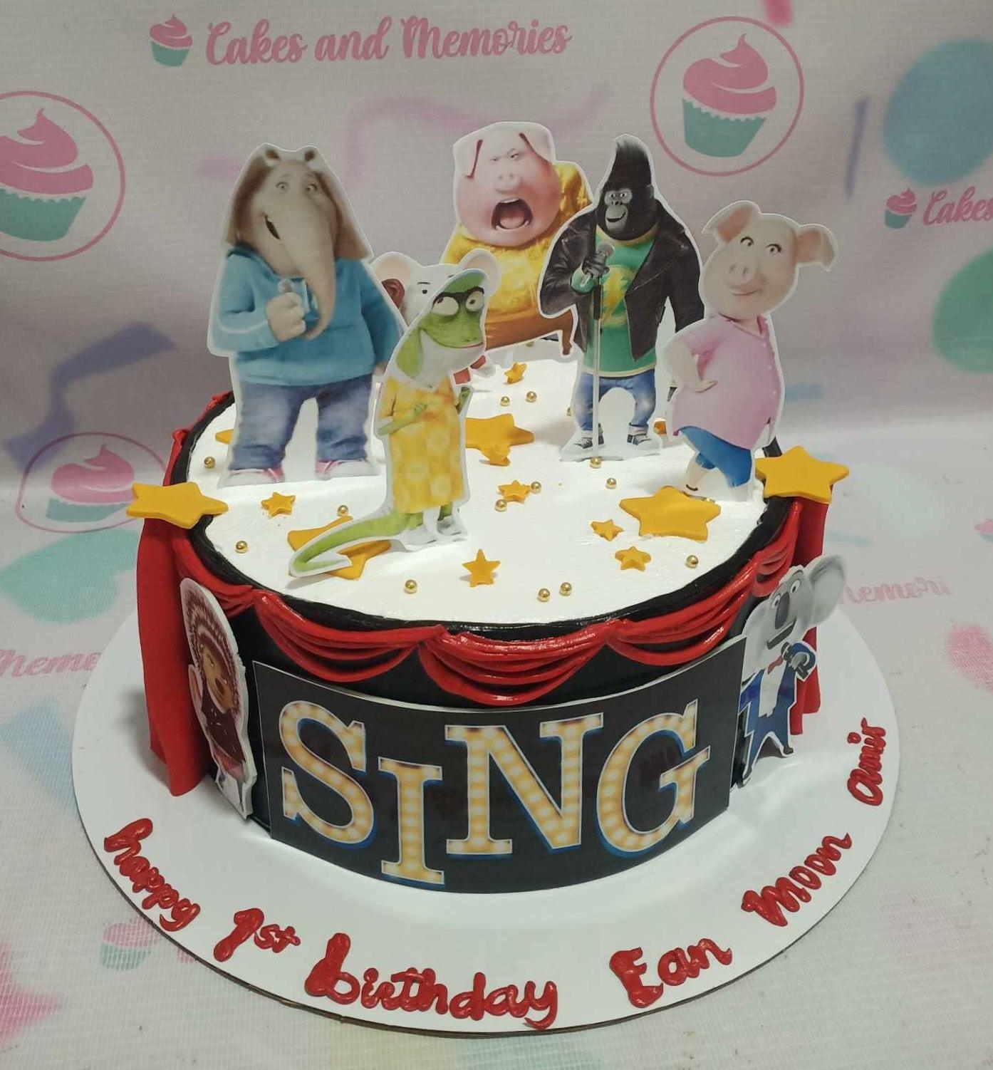 Sing movie themed birthday cake with character printouts, red icing drapes, and gold stars on a black and white base.