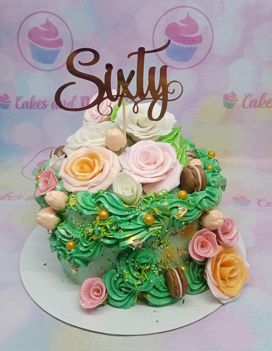 Floral 60th birthday cake with green icing rosettes, pink and peach sugar roses, and a rose gold Sixty topper.