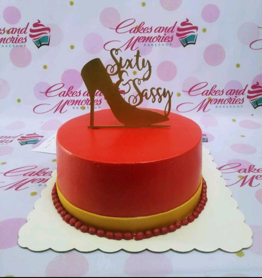 Red minimalist birthday cake with a gold high heel shoe topper and 'Sixty & Sassy' message.