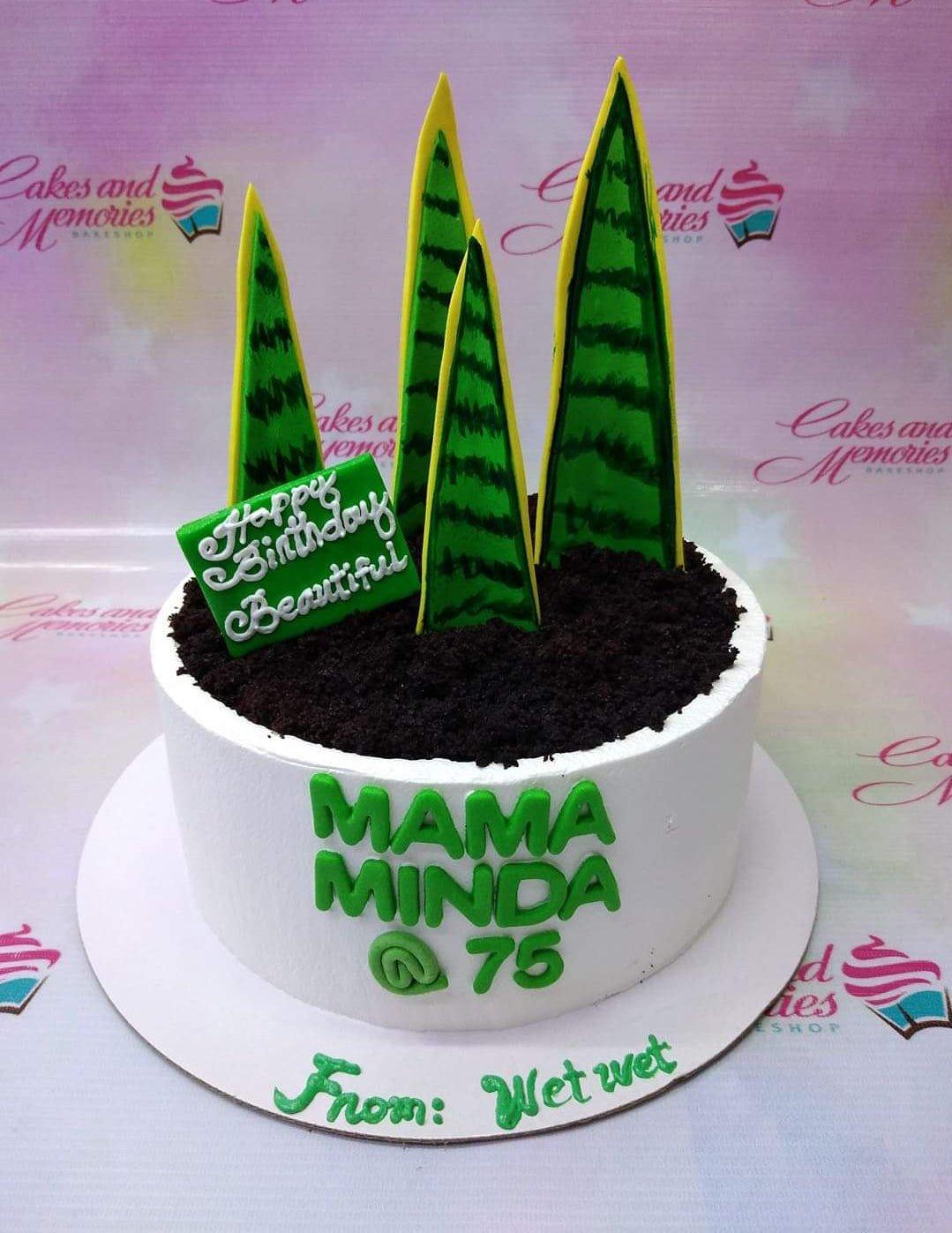 White round cake with dark chocolate soil topping and tall green snake plant fondant toppers for a 75th birthday celebration.