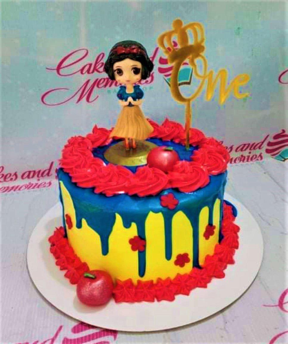 Snow White themed birthday cake with yellow icing, blue drip, red rosettes, and a Snow White figurine on top.
