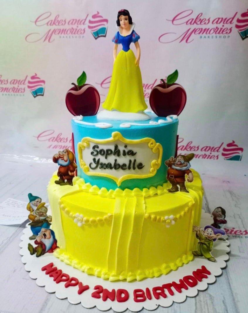 Two-tier Snow White themed birthday cake with yellow and blue icing, featuring Snow White and the Seven Dwarfs toppers.