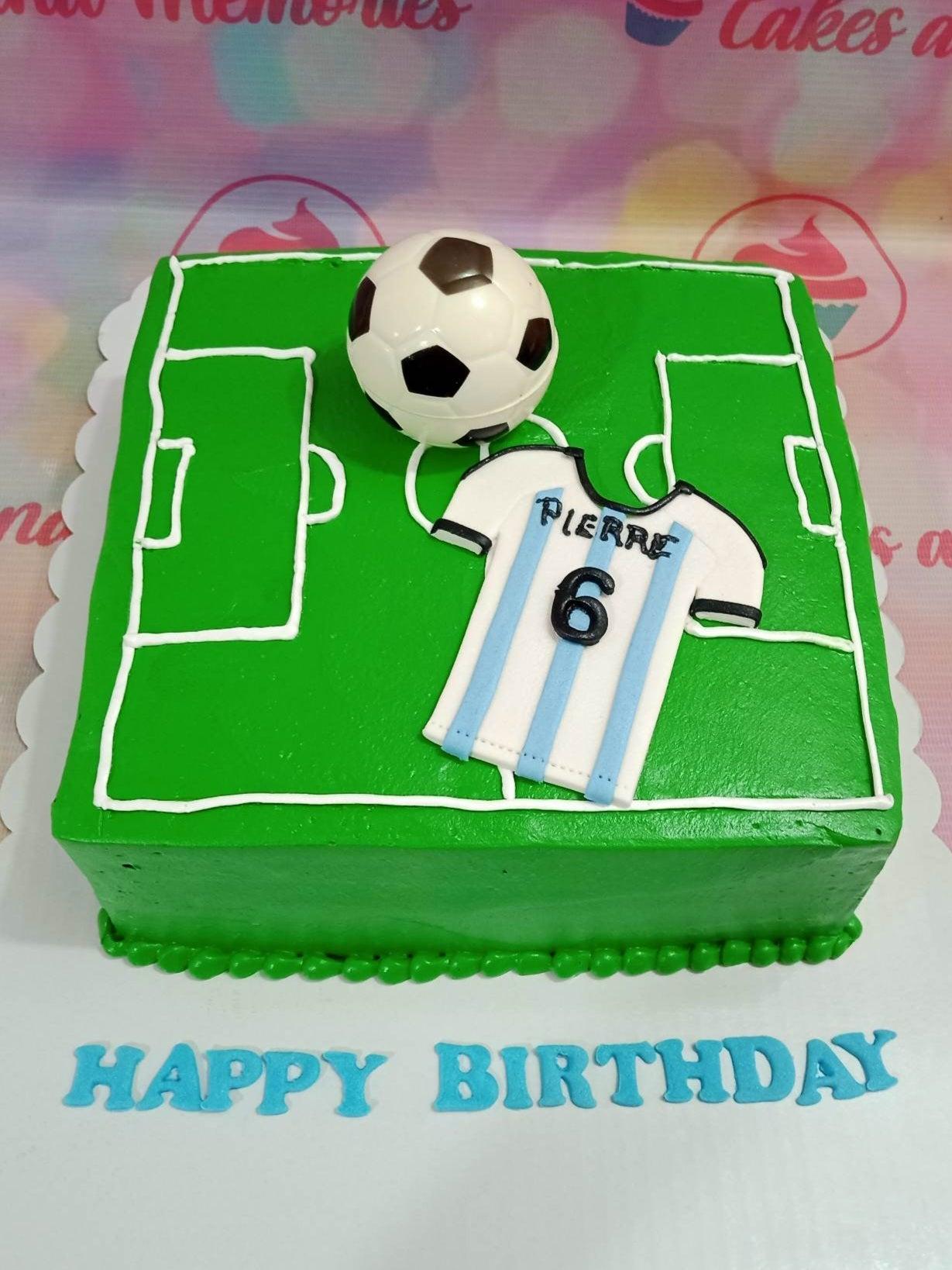Square green soccer field cake with a 3D soccer ball, a blue and white striped jersey topper, and a Happy Birthday message.