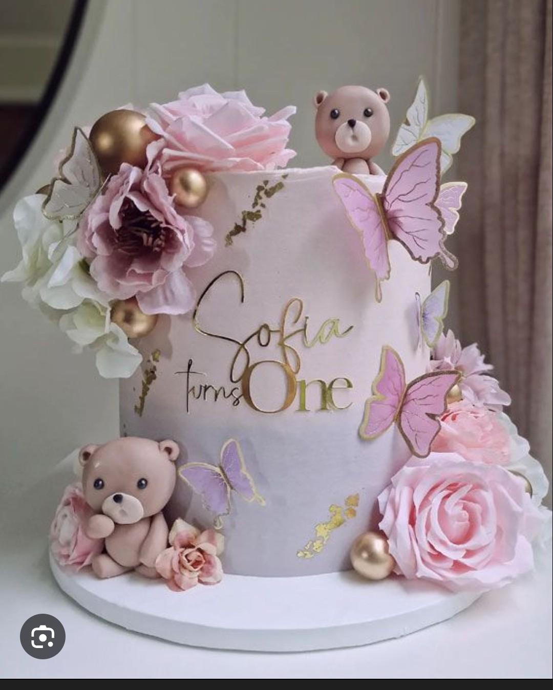 Pink and purple ombre cake with fondant bears, pink roses, gold spheres, and purple butterflies for a first birthday.