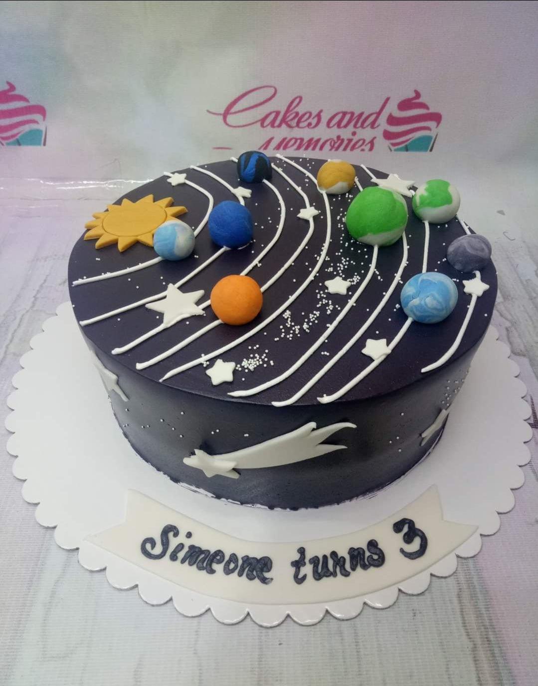 Solar system themed birthday cake with dark purple icing, fondant planets, a sun, and a shooting star for a 3rd birthday.