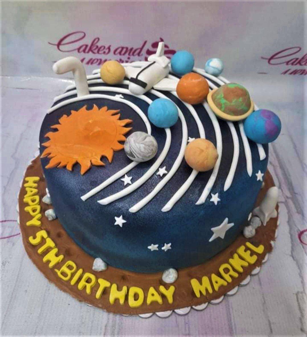 Solar system themed birthday cake with fondant planets, a space shuttle, and a large sun on a dark blue galaxy background.