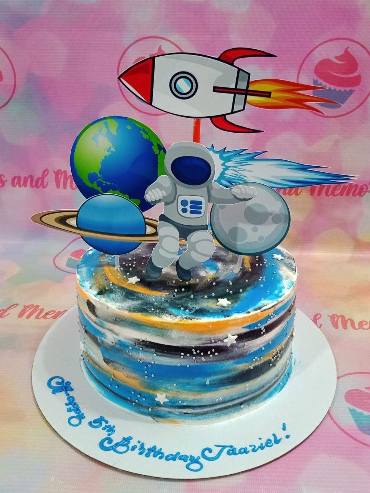 Space themed birthday cake with astronaut, rocket, and planet printouts on a galaxy-style blue and orange icing base.