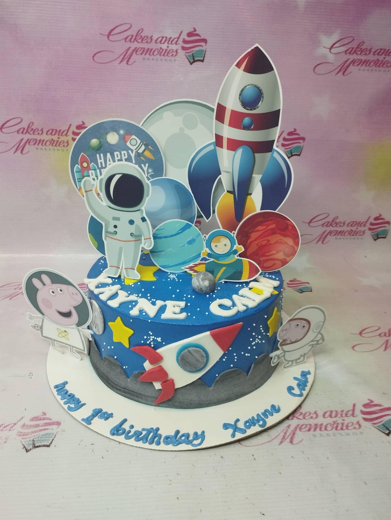 Blue space themed birthday cake with astronaut, rocket, and planet printouts and white icing stars.