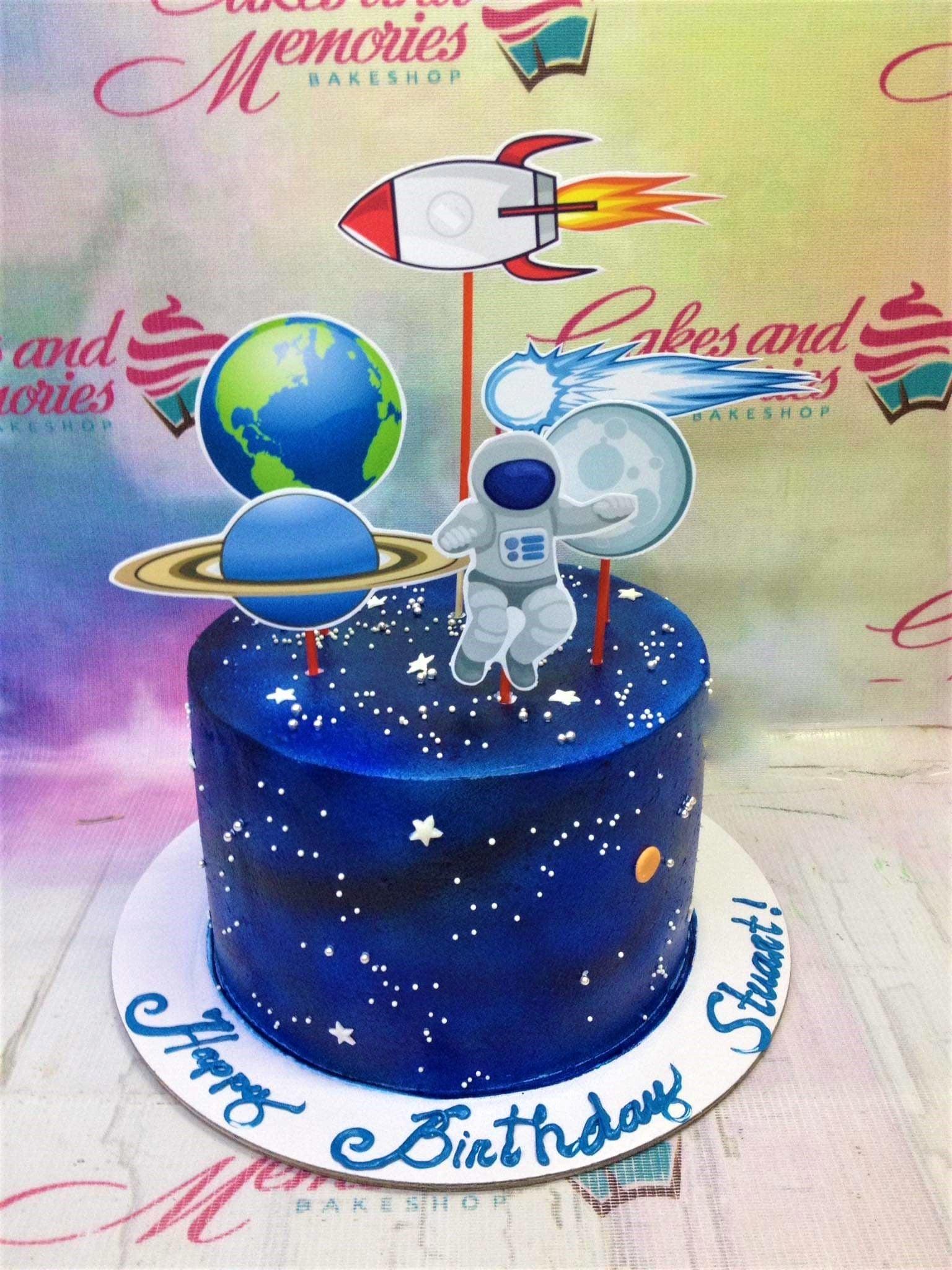 Deep blue space themed birthday cake with astronaut, rocket, and planet toppers and silver star sprinkles.