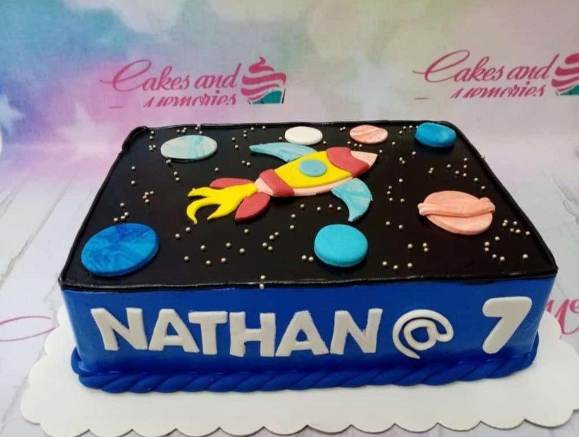 Space themed rectangle cake with a blue base and black top featuring a fondant rocket ship, planets, and silver dragees stars.