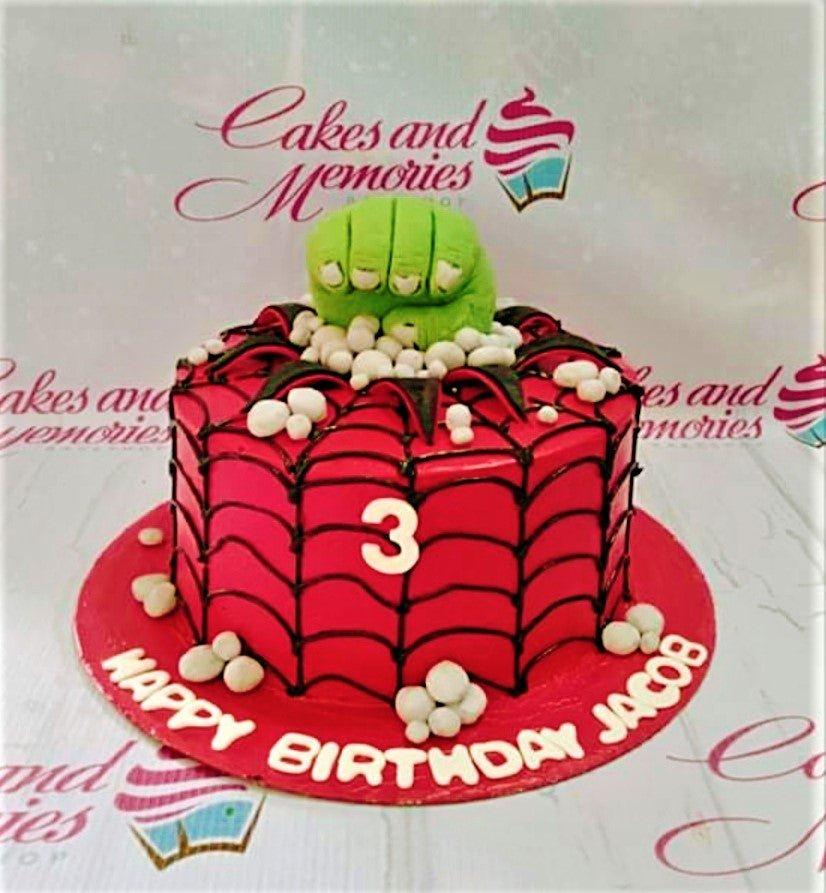 Red Spiderman-themed birthday cake with a green Hulk fist topper and black web icing design.
